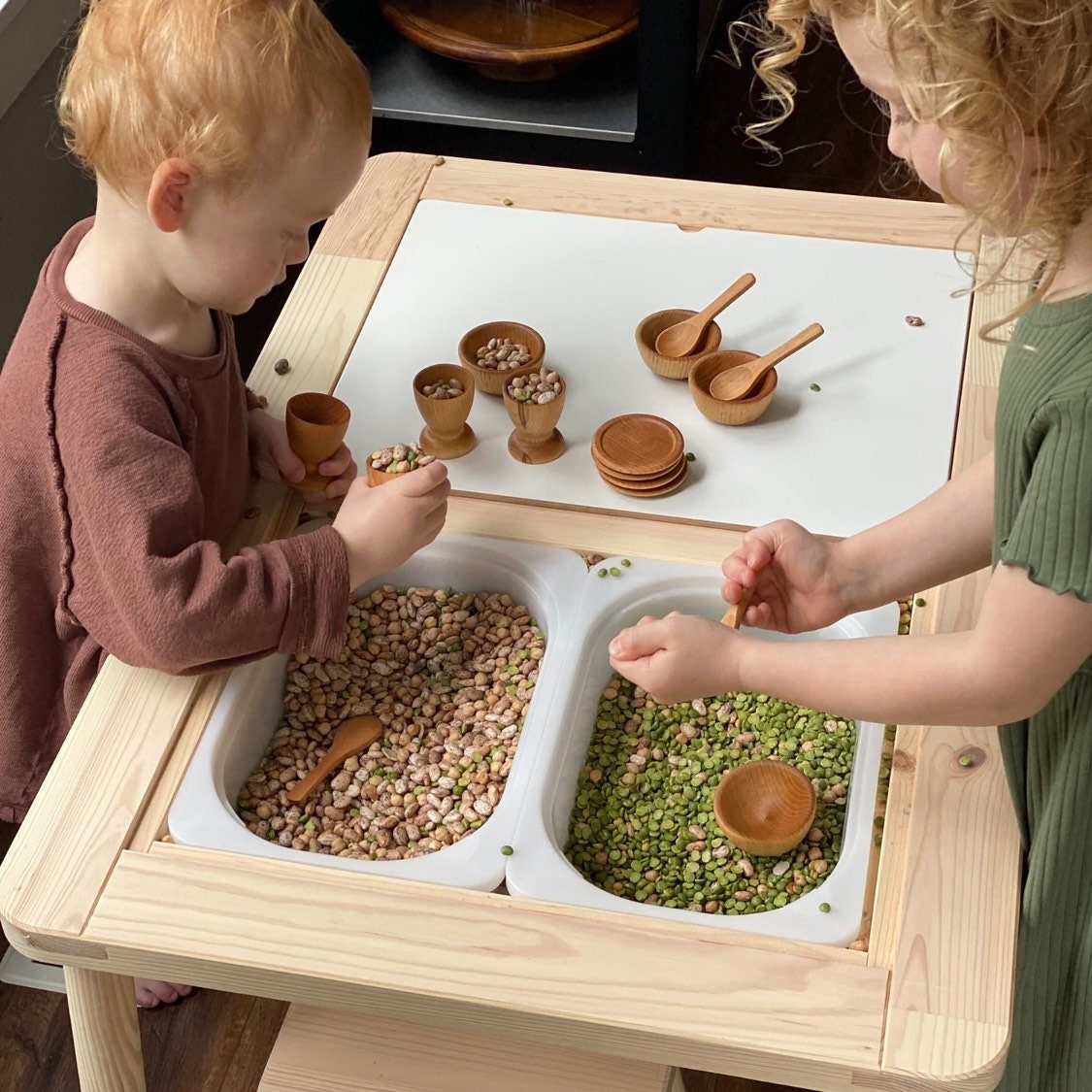 Children using wooden dish set in a sensory table as scoops. Play dish set